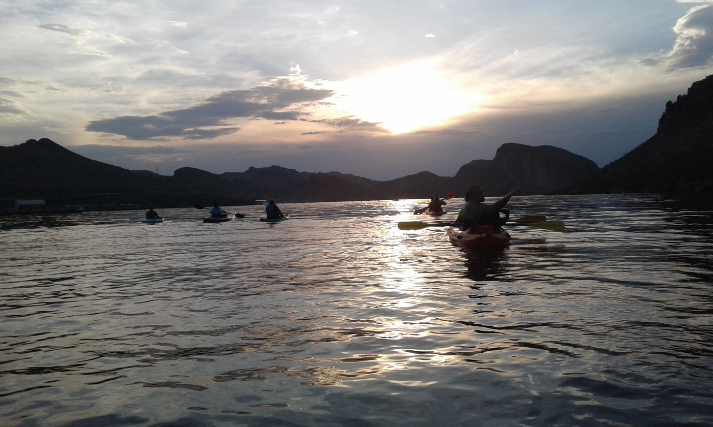 Kayakers paddling into the sunset with mountains behind